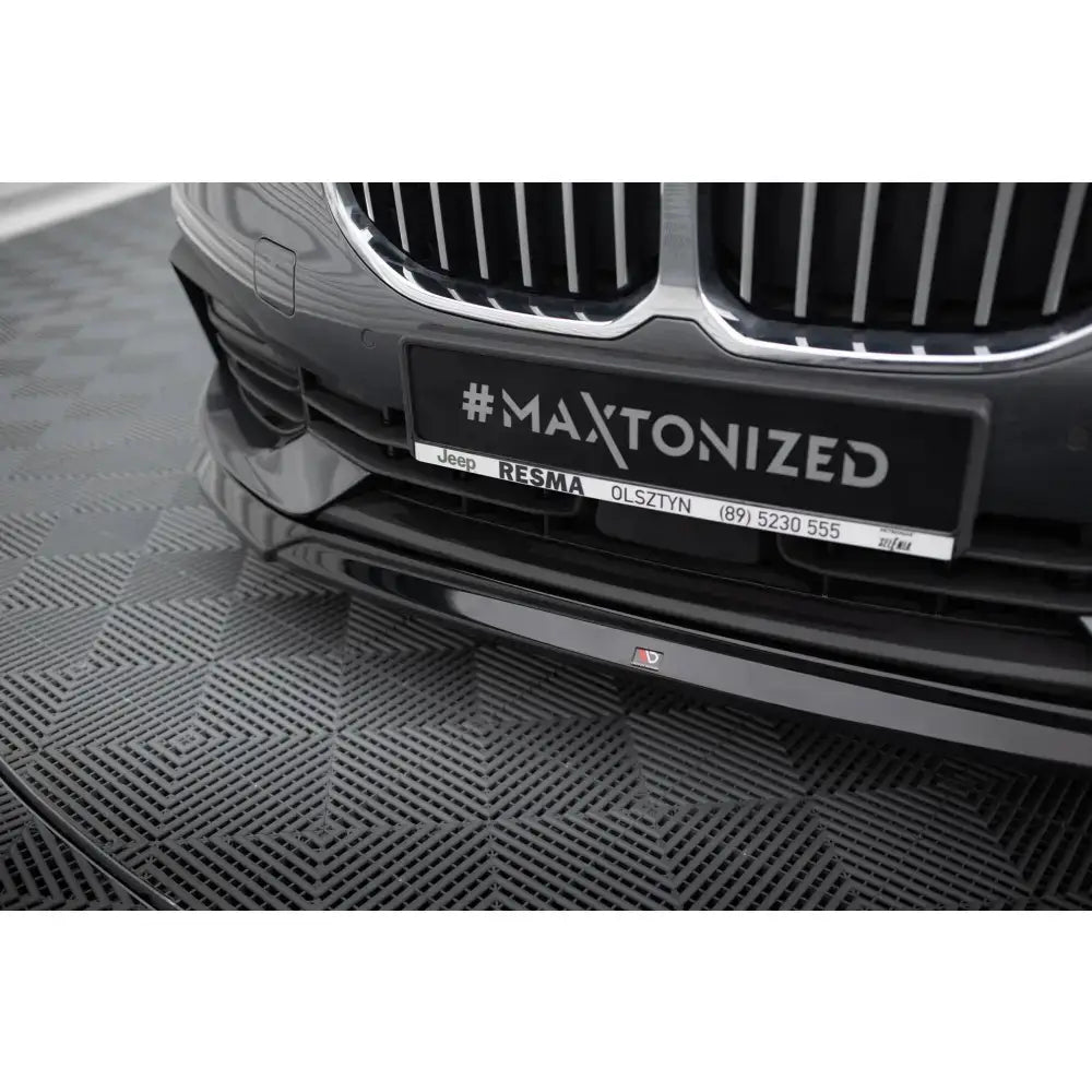 Front lip på BMW 1 F40 V.2, sort blank spoiler sett fra lav vinkel mot gittermønstret gulv.