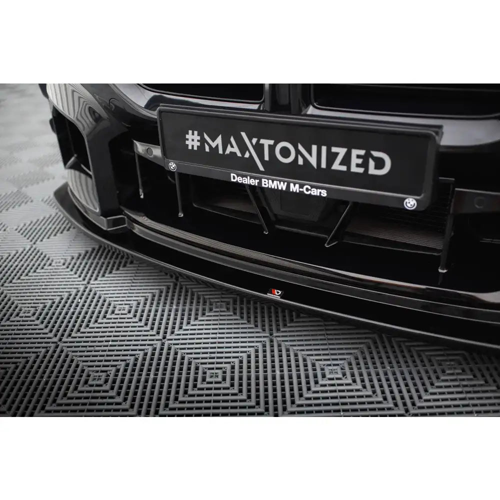 Front splitter på BMW M2 G87 V.4 i sort blank finish med #MAXTONIZED skilt, sett forfra fra lav vinkel.