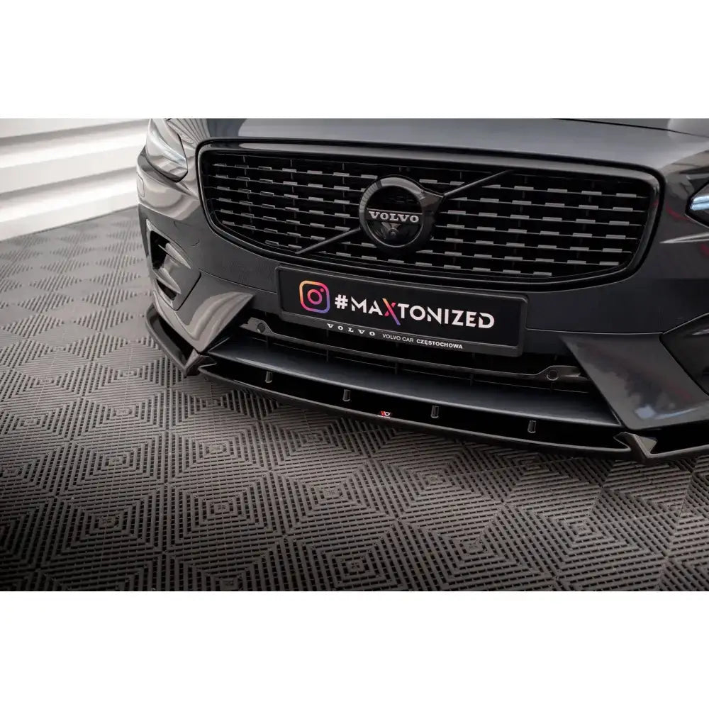 Front splitter på svart plastspoiler montert på Volvo V90 R-Design, sett forfra med grill og #MAXTONIZED-skilt.