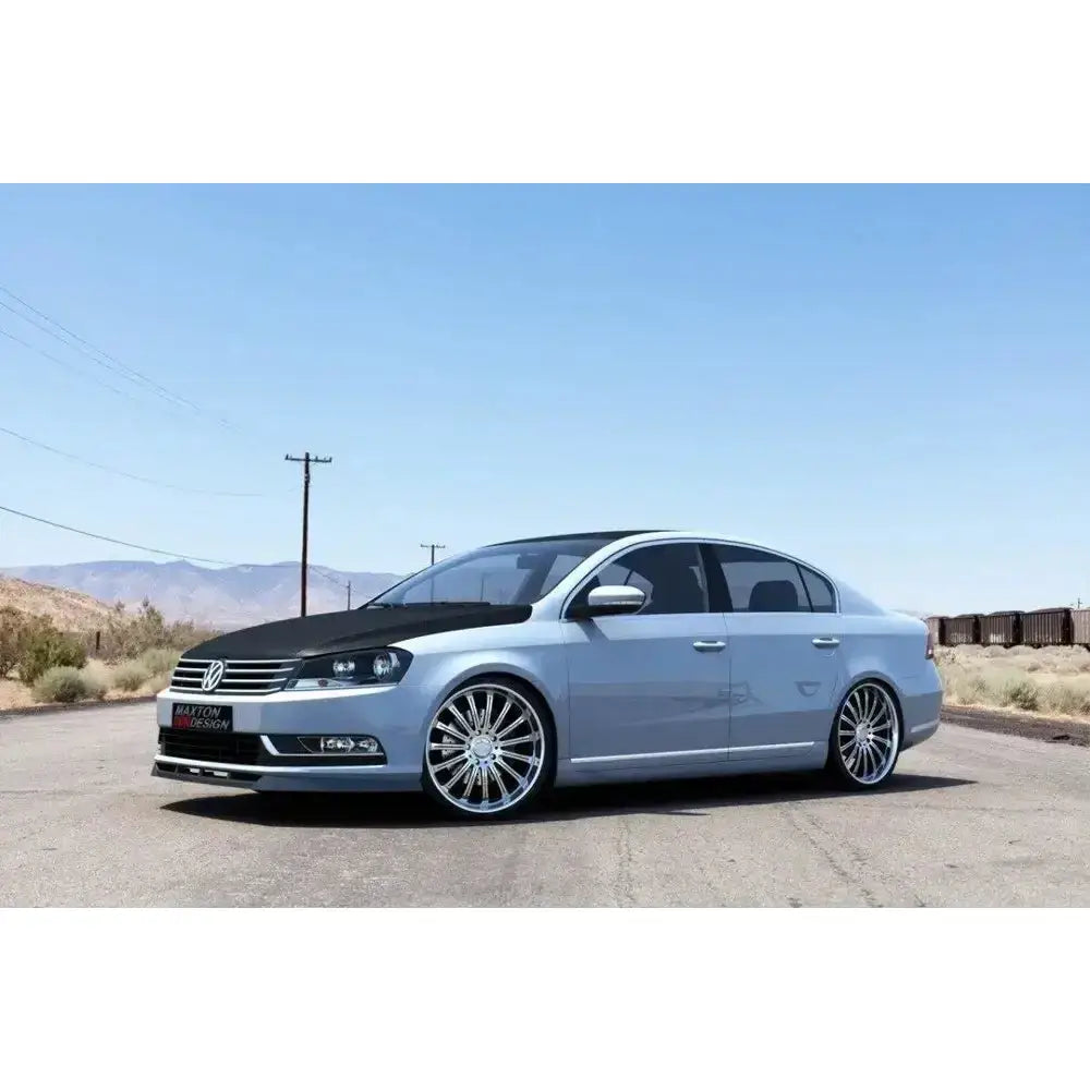 Frontspoiler VW Passat B7 sølv sedan med sotede ruter og sorte detaljer, parkert i solfylt landskap.