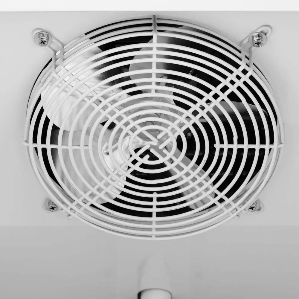 Ventilasjonsvifte på fryseskap med lås og glassdør, nærbilde av hvitt metallgitter og festeskruer.