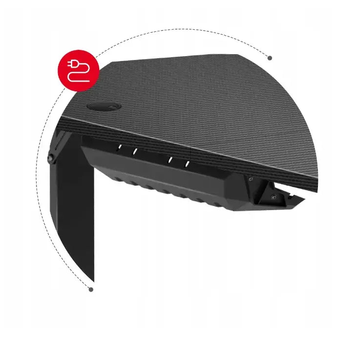 Gamingbord Huzaro Hero 4.7, nærbilde av svart bordhjørne med kabelhull og rød strømplugg-ikon på undersiden.