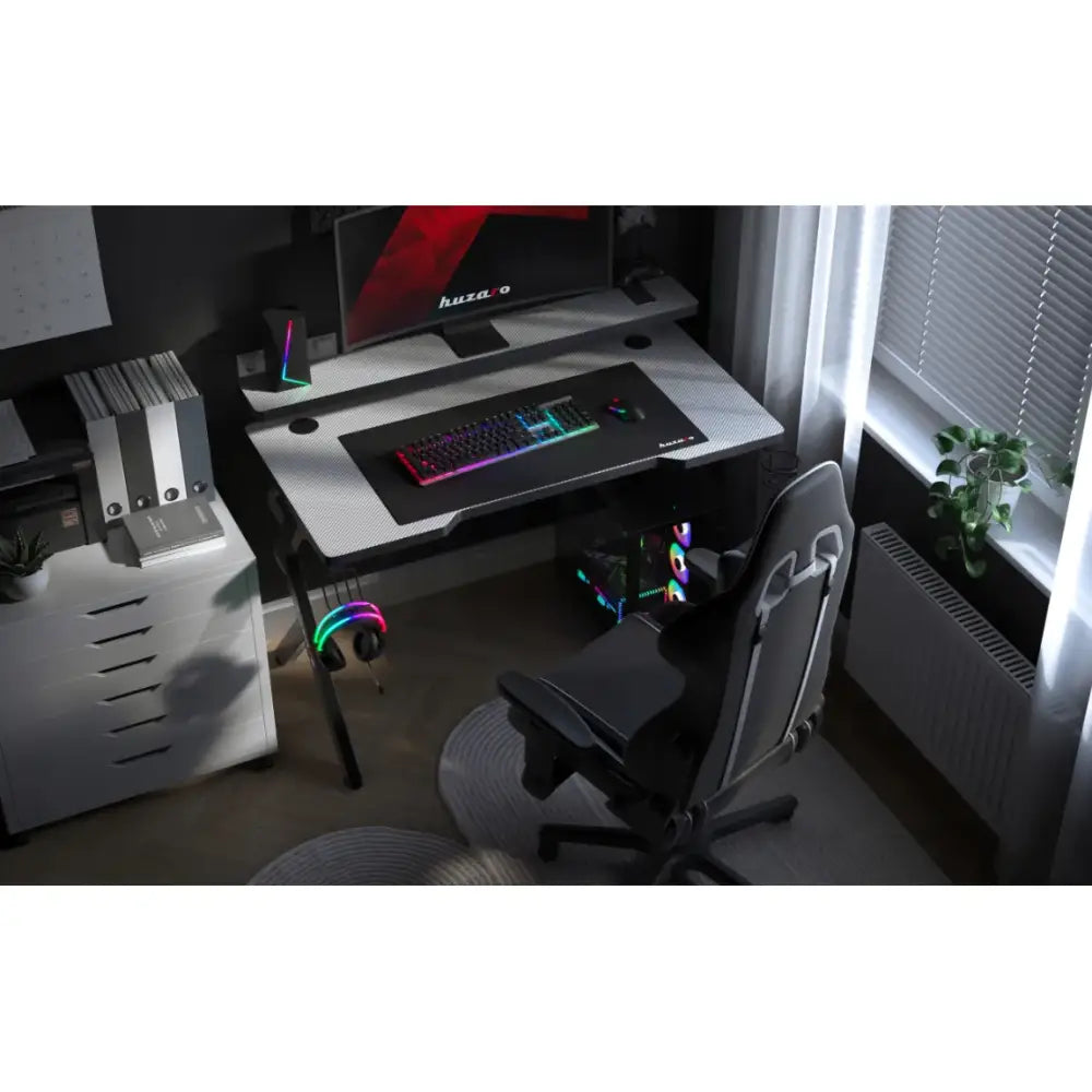 Gamingbord Huzaro Hero 5.0 hvit, sett ovenfra med RGB-tastatur, skjerm og svart ergonomisk gamingstol.