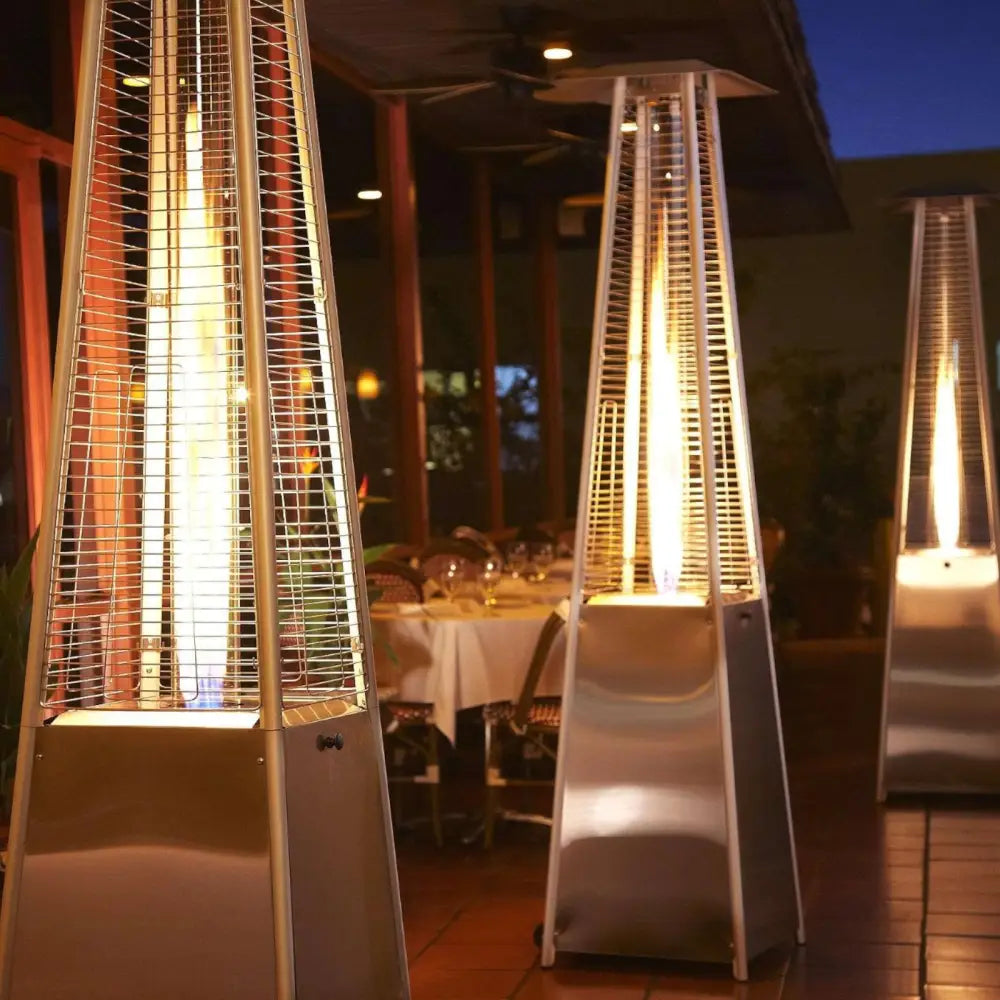 Gassovn Glass Pipe terrassevarmere i metall, trekantet design, synlig flamme i kveldslys, flere enheter på rekke.