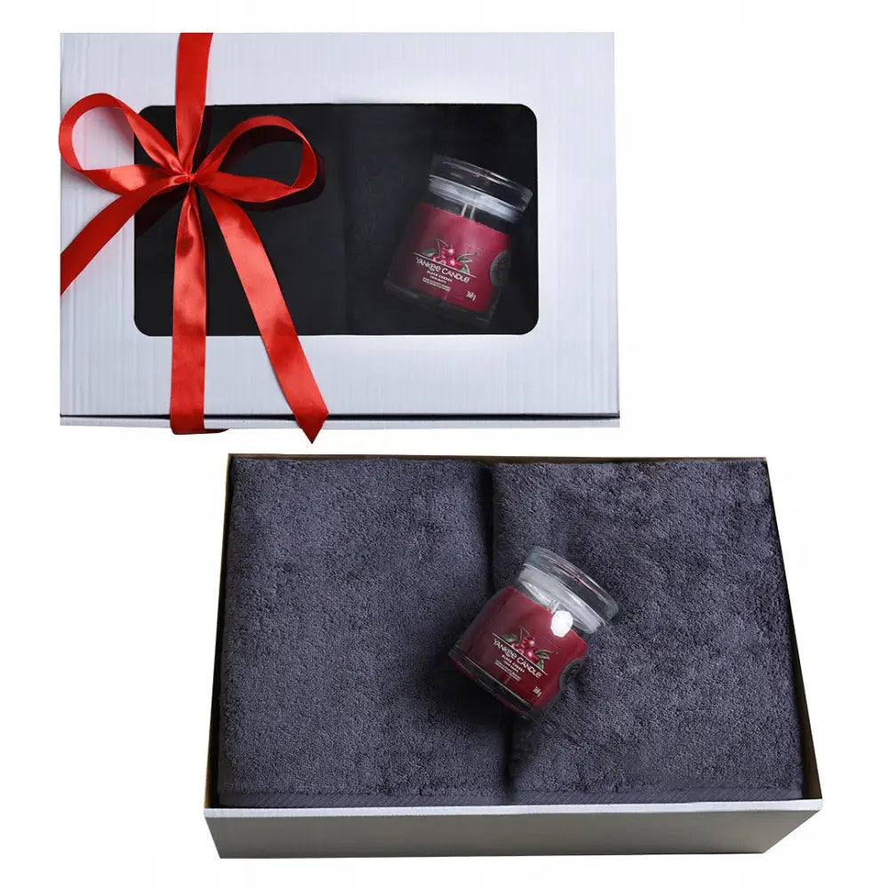 Gavesett med to mørkegrå badehåndklær og rødt Yankee duftlys i glass, pyntet med rød silkebånd i gaveeske.