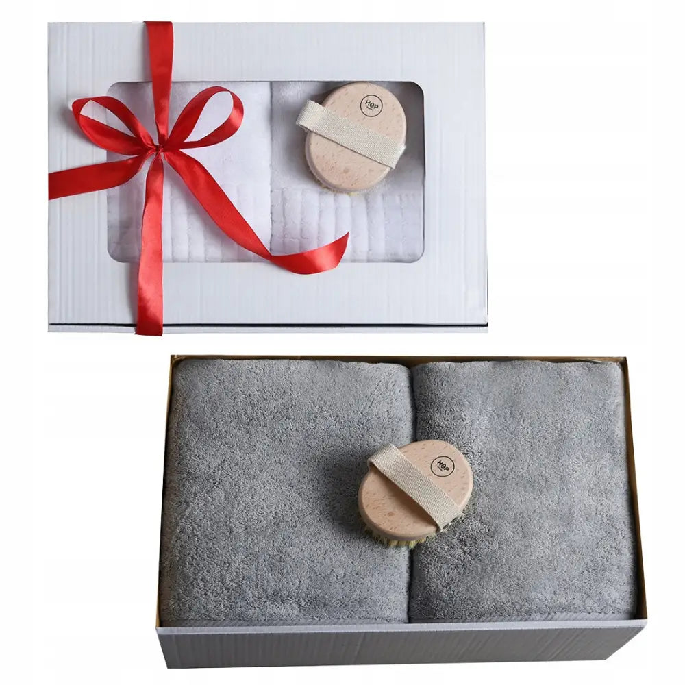 Gavepakke med to grå håndklær og rund massasjebørste, elegant pakket i eske med rødt silkebånd.