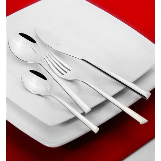 Gerlach Flames bestikksett med kniv, gaffel, spiseskje og teskje diagonalt på hvite tallerkener mot rød bakgrunn.