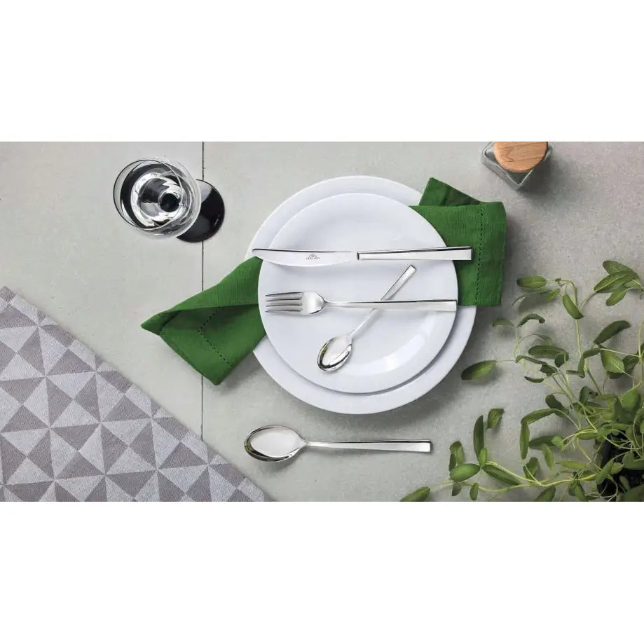 Gerlach Onda bestikksett på hvite tallerkener, grønn serviett og grått mønstret underlag med grønne planter.