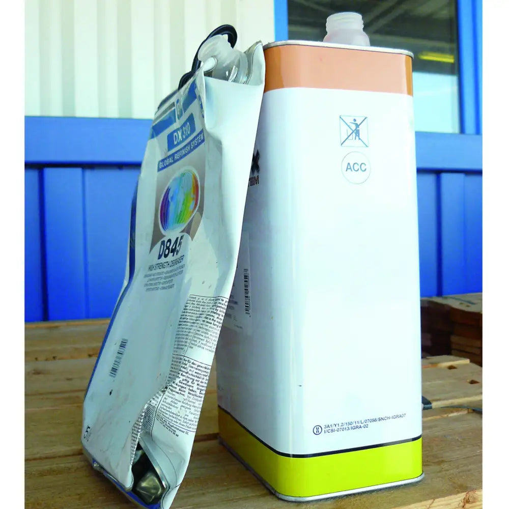 Gjenvinningspresse til store metallbokser, sammenklemt og hel kanne ved siden av hverandre på trebord.