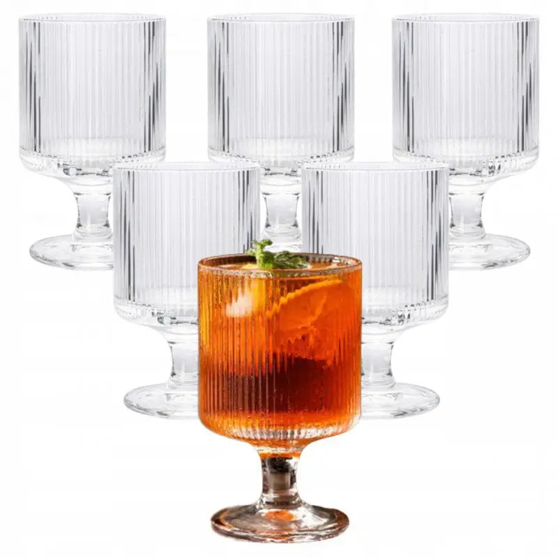 Dessertglass med riflet design på stett, ett fylt med oransje drikke, isbiter og sitronskive.