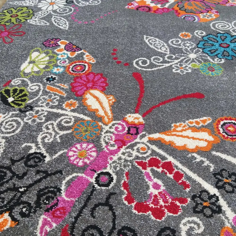 Grå rektangulært teppe med fargerikt sommerfuglmotiv, nærbilde av rosa, blå og oransje blomsterdetaljer.