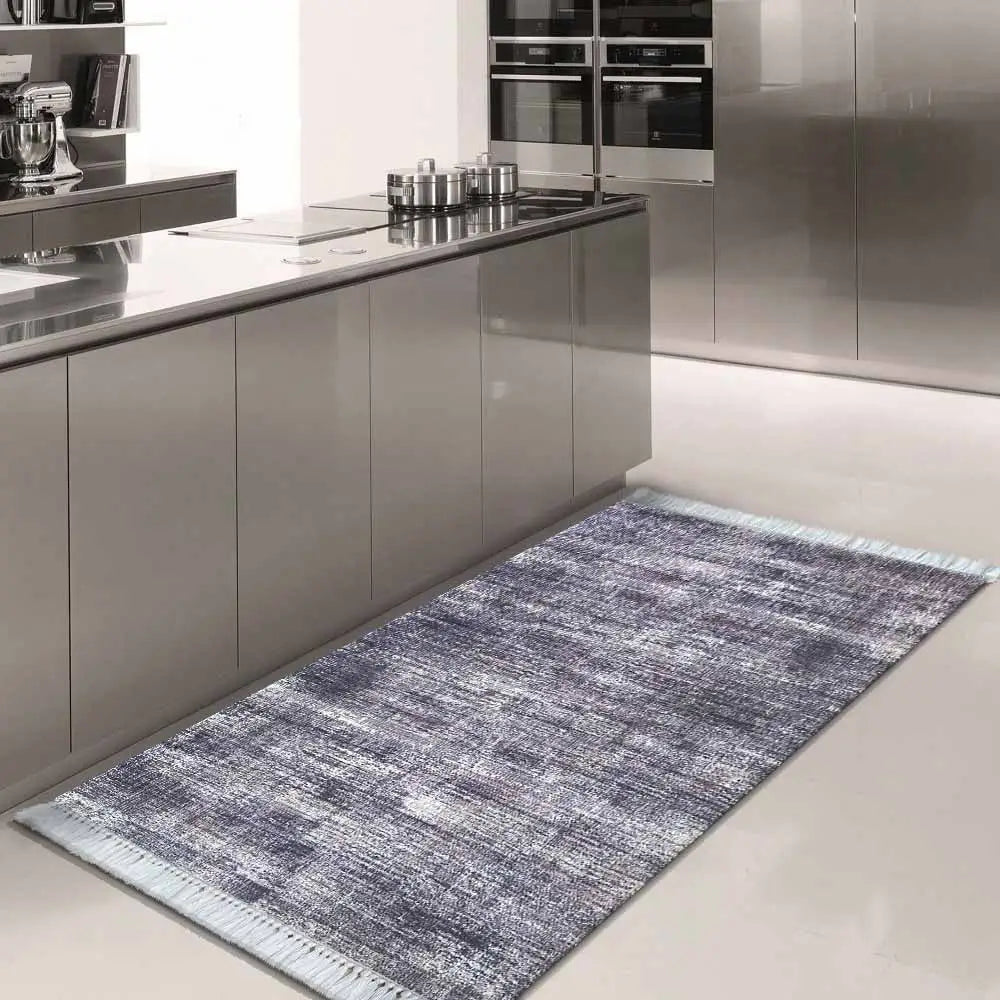Grått og blått teppe 160 x 220 cm med sklisikker bunn, lagt foran kjøkkenskap i stål på lyst gulv.