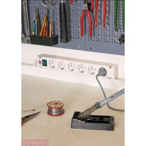 Grenuttak med seks uttak og grønn bryter montert på verkstedvegg, loddebolt og tenger synlig i bakgrunnen.