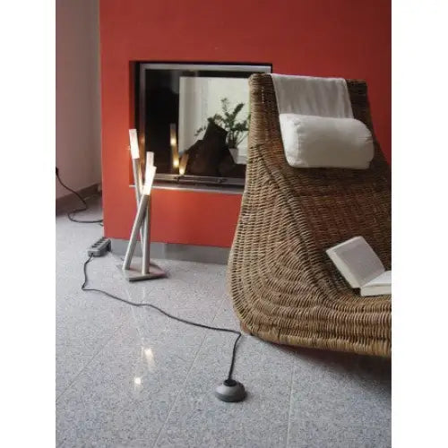 Stol i flettet naturmateriale med hvit nakkepute, åpen bok på setet og rød vegg i bakgrunnen.