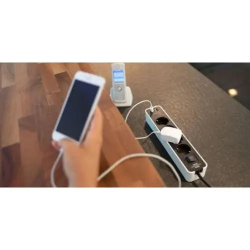 Grenuttak Ecolor 4-veis hvit/svart, skråvisning med to stikkontakter og USB-uttak i bruk med ladende enheter.