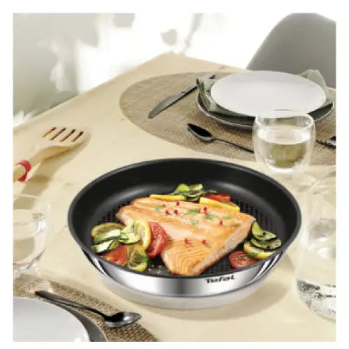 Stekepanne fra Ingenio Emotion sett, fylt med laks og grønnsaker, plassert på et dekket middagsbord.