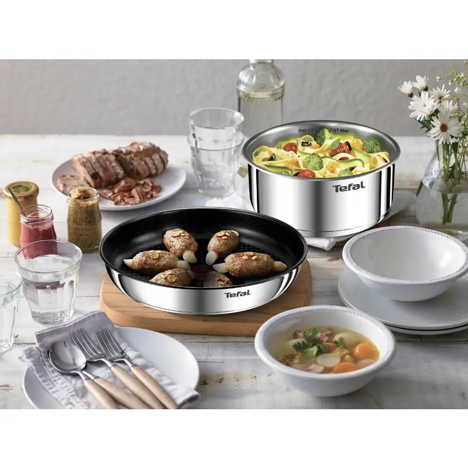 Gryter og Panner Ingenio Emotion sett, to kasseroller fylt med mat på lyst dekket bord med serveringsutstyr.