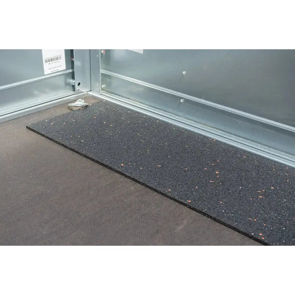 Gulvmatte i svart gummi med fargede prikker, nærbilde av teksturert overflate i hjørnet av metallskap.