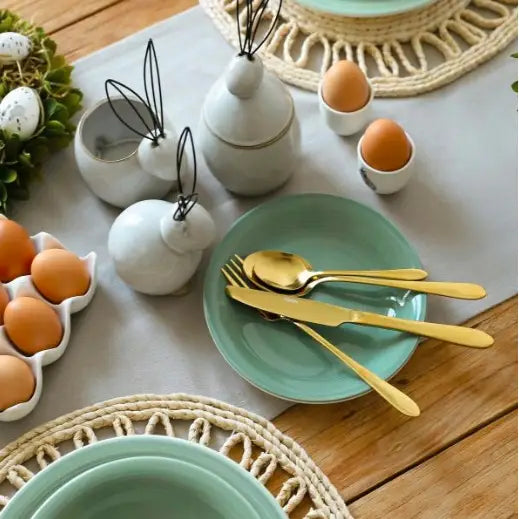 Gylne bestikk fra Homla, elegant dekket bord med pastellgrønne tallerkener og keramiske figurer.