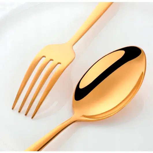 Gylne bestikk i rustfritt stål, gaffel og skje sett ovenfra på hvit tallerken med blank finish.