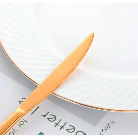 Gyllent bestikk, nærbilde av knivblad på hvit tallerken med rillet kant og elegant gullkant.