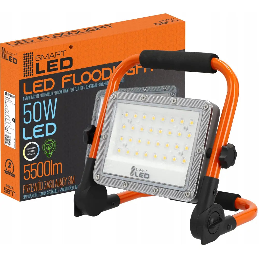 LED arbeidslampe på stativ med oransje ramme og sort håndtak, sett skrått foran original emballasje.