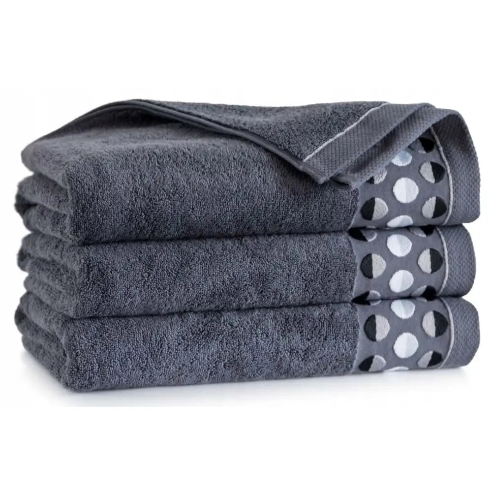 Fire mørkegrå Zwoltex Zen_2 bomullshåndklær, sidevisning av stabel med prikkete grå og hvit kantdekor.