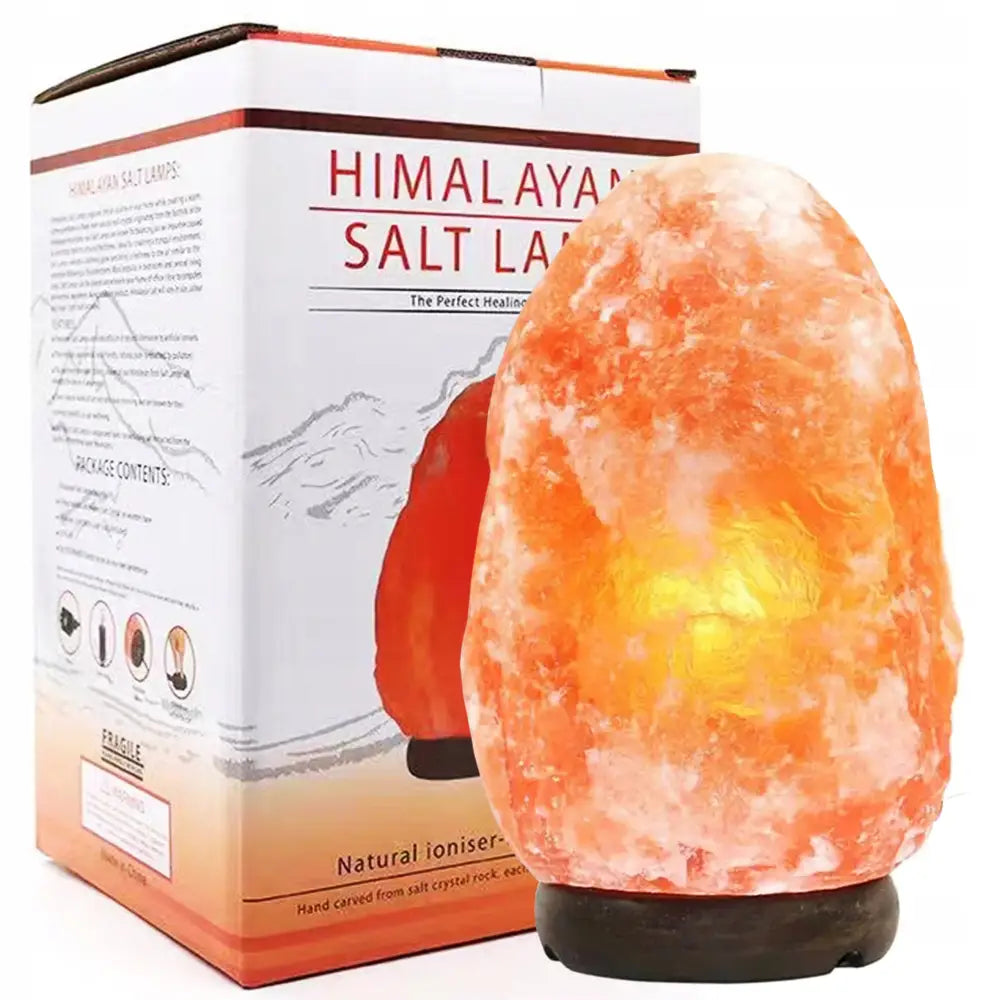 Himalayasaltlampe som lyser varmt, ujenv overflate og eske synlig bak på mørkt underlag.