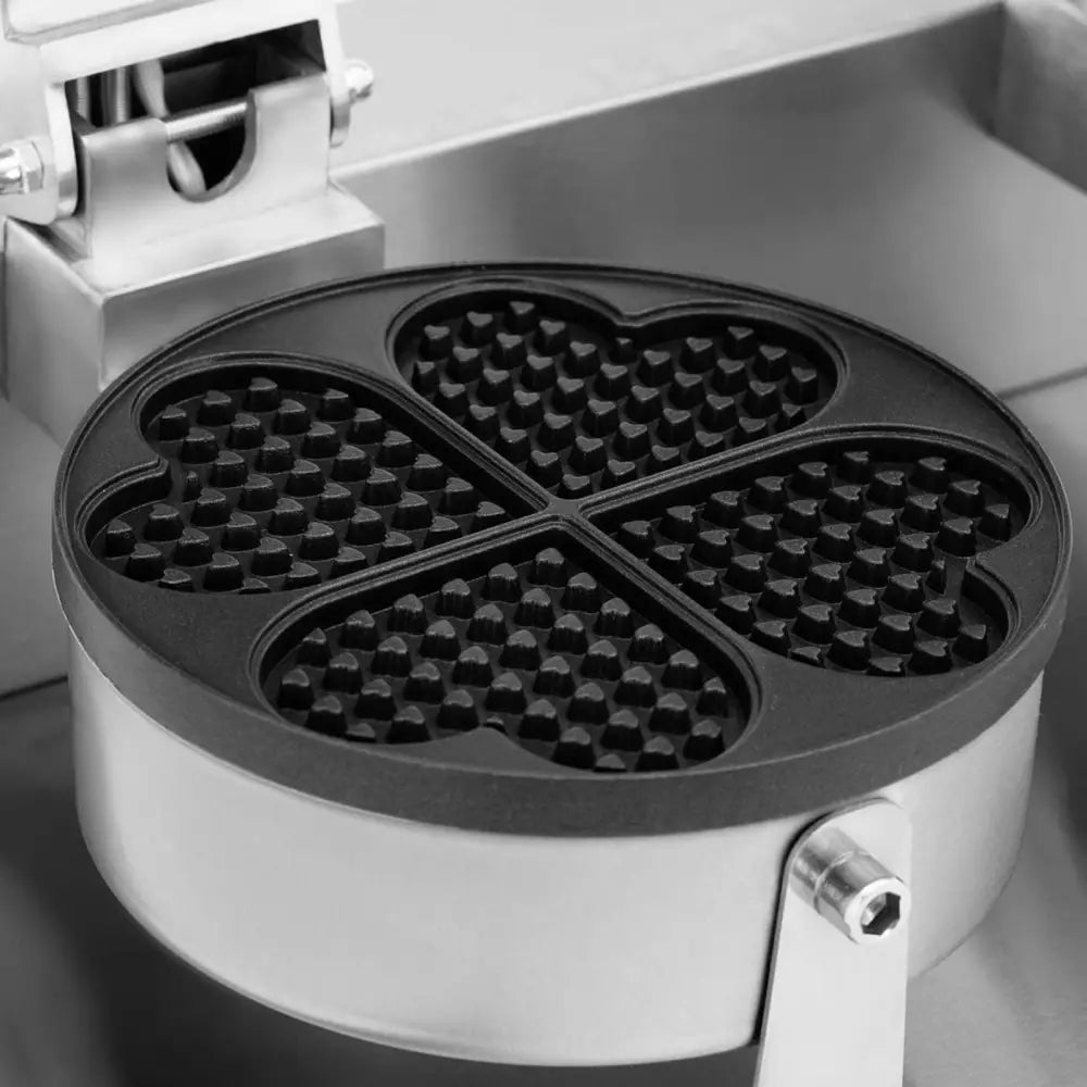 Hjerteformet dobbelt vaffeljern med fire dype plater, nærbilde fra skrå vinkel viser rutemønster og metall.