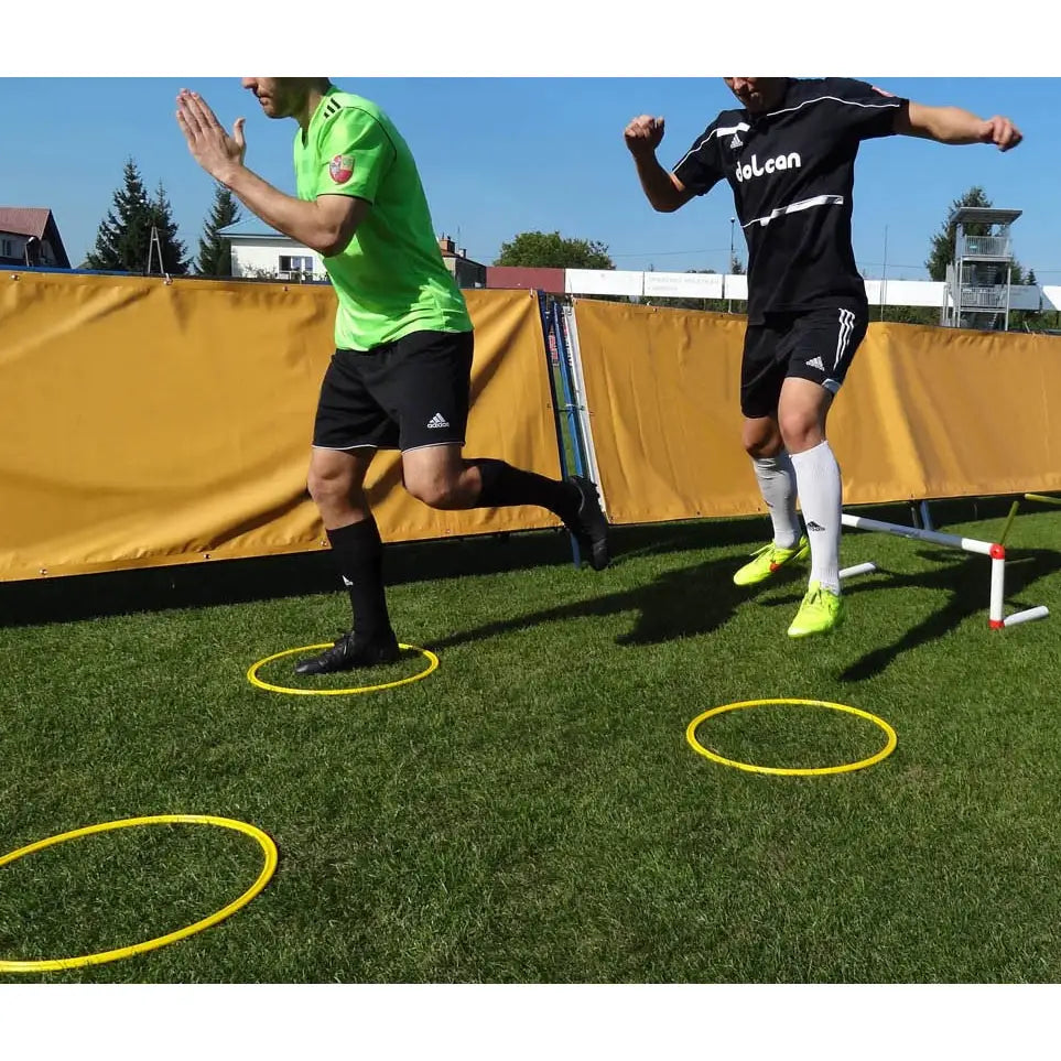 Hjul koordineringssett brukt utendørs, to personer hopper mellom gule plastringer på gress under trening.