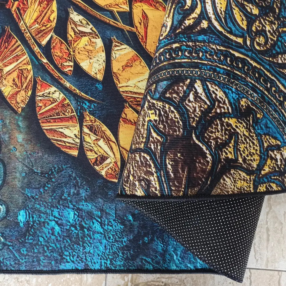 Horeca Nytt teppe, nærbilde av fargerikt blad- og mønsterdesign, oppbrettet bakside med antiskli-nupper.