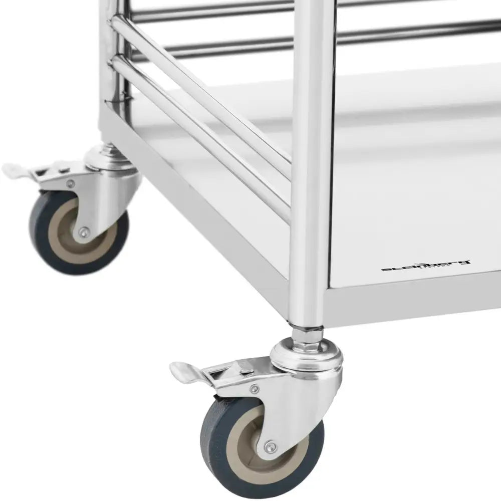 Servicetralle i stål, nærbilde av blanke hjørner med to grå, dreibare hjul og synlige bremsepedaler.