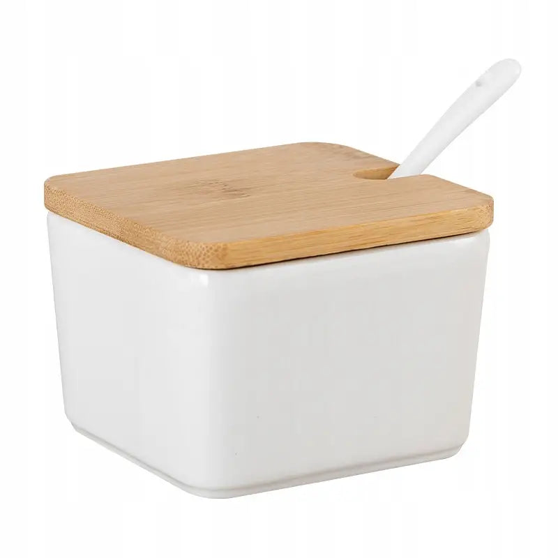 Hvit sukkerbøtte i porselen med bambuslokk og hvit skje, sett skrått med utsparing til skjeen.