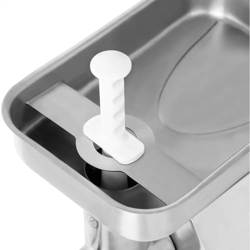 Industriell kjøttkvern, nærbilde av rustfri overflate med hvitt håndtak festet i rundt hull ved kanten.