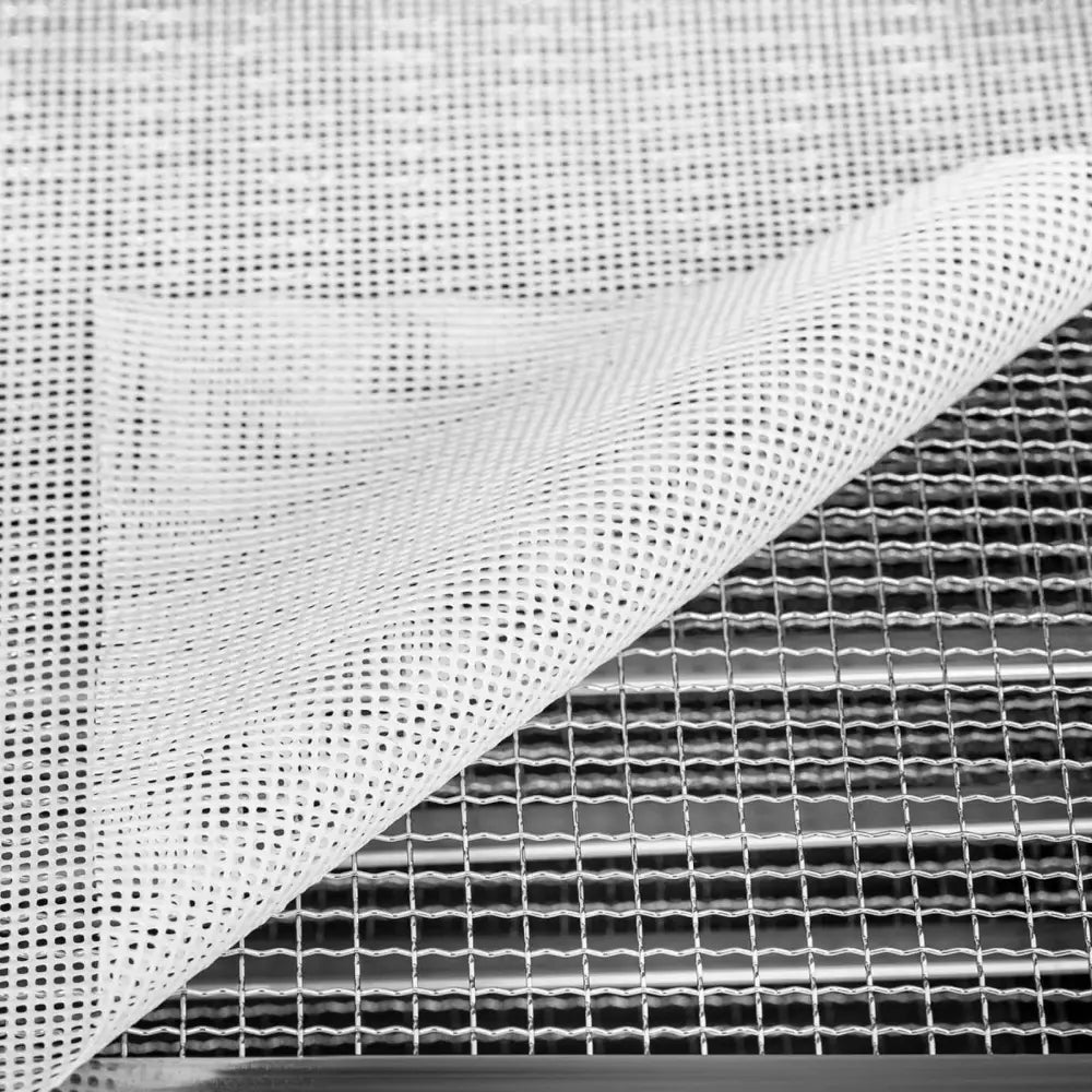 Industriell mat dehydrator, nærbilde av hvitt nettingstoff løftet for å vise metallgitter og perforeringer.