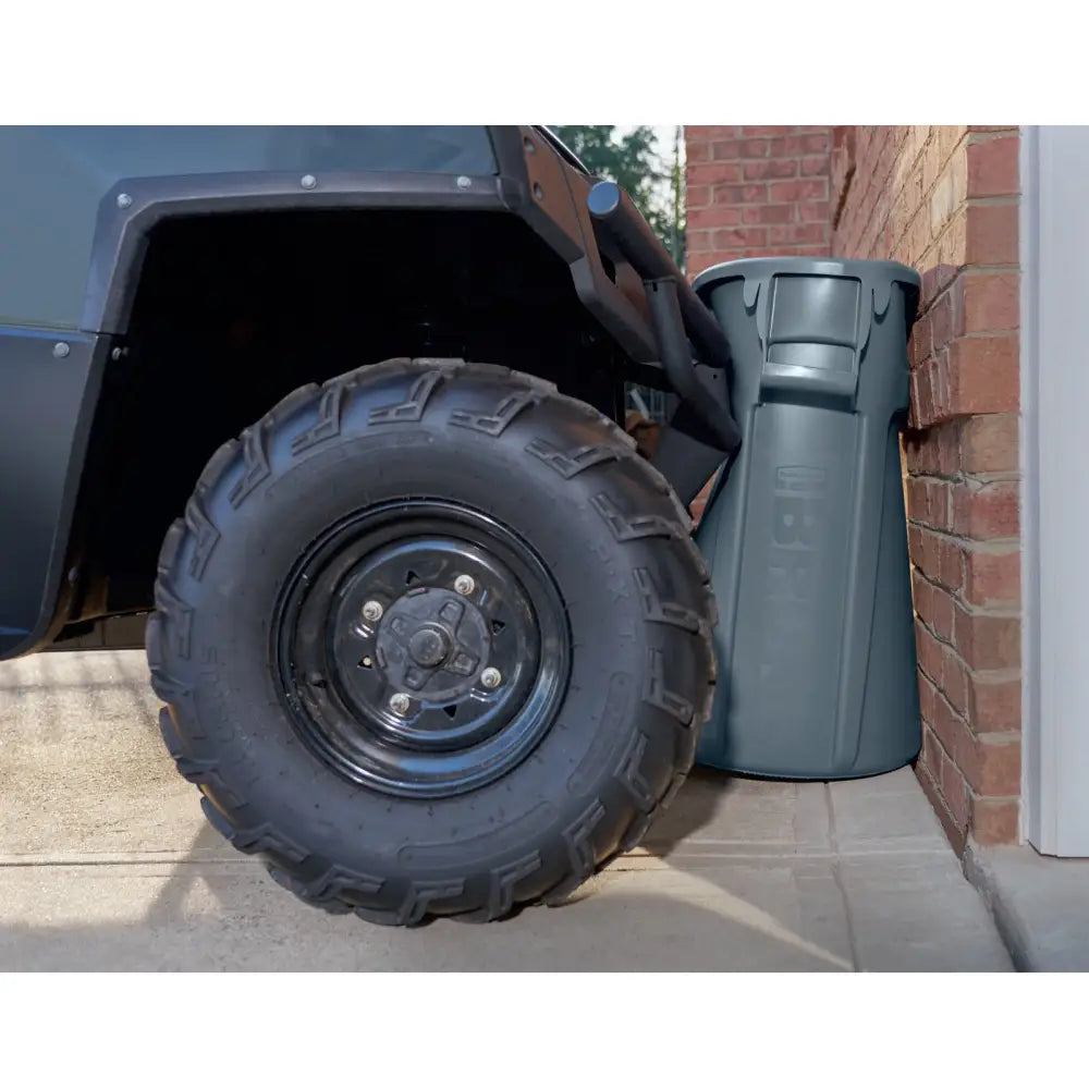 Industriell BRUTE Round 166L avfallsbeholder i mørk grå plast, vist ved murvegg med robust hjul ved siden av.