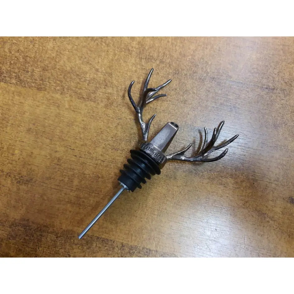 Jägermeister tappeapparat med hjortehorn, nærbilde av metallisk helletut med sorte gummiriller på trefarget bakgrunn.