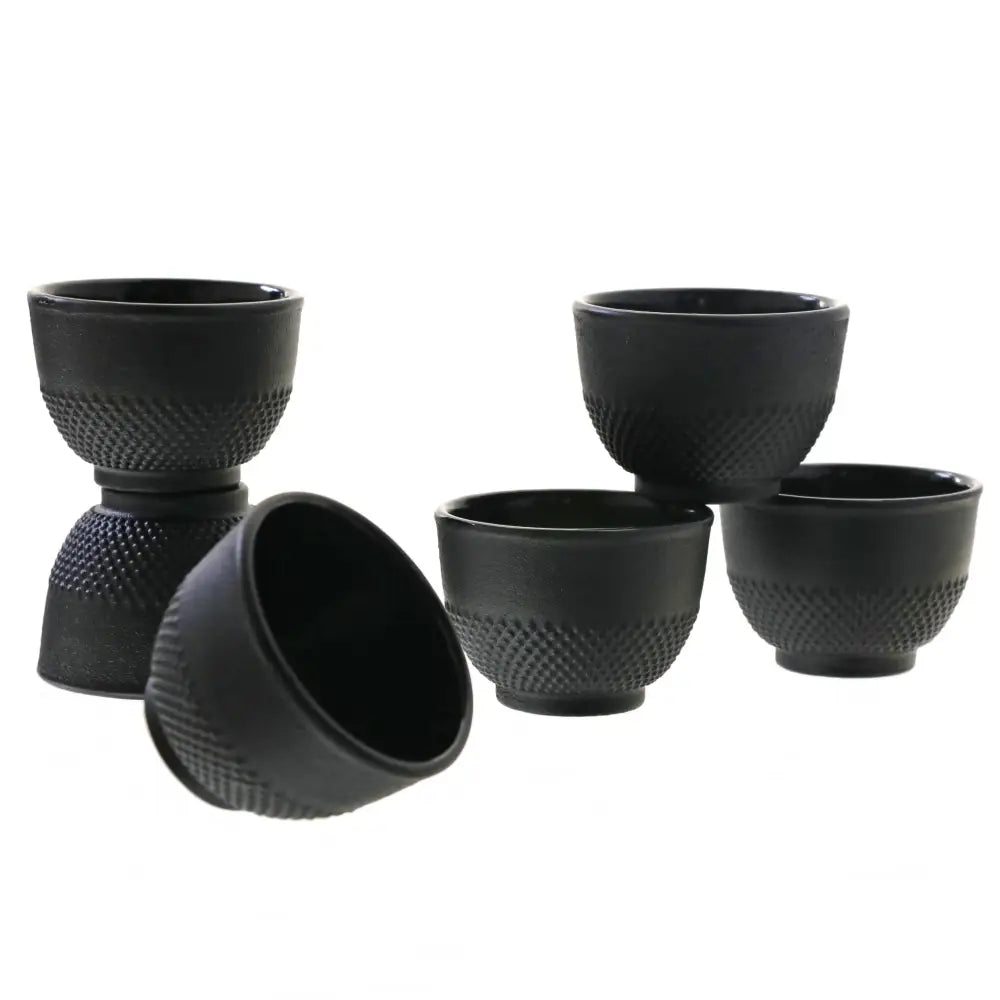 Jern tekopper, fem sorte metallskåler med teksturert overflate, én liggende og fire stående mot hvit bakgrunn.