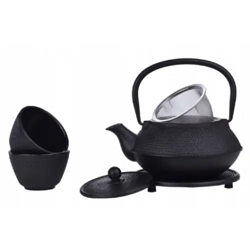 Jern tepotte sett med sort tekanne i støpejern, bøylehåndtak, stablede kopper og løst lokk foran.