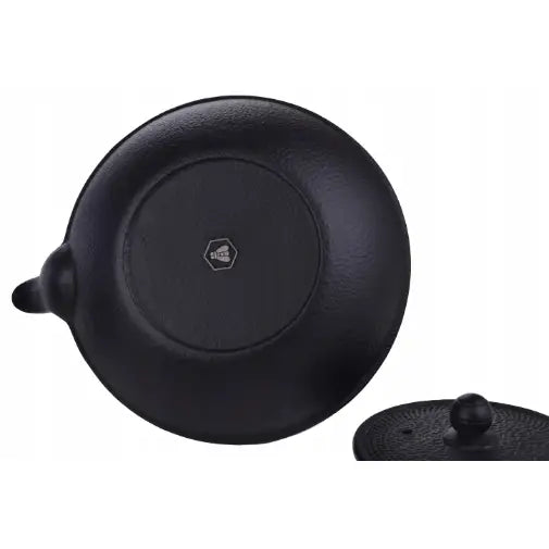 Jern tepotte sett, underside av sort støpejernsgryte med synlig helletut og delvis lokk nederst i bildet.