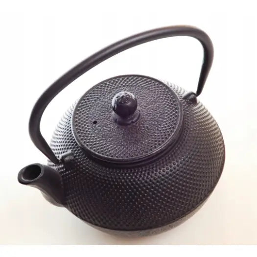 Jernkanne med sil, sett rett ovenfra, viser rillet støpejernsoverflate, buet håndtak og avrundet lokk.