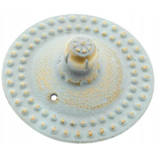 Jernkanne tevannkoker, lyseblå rund metallskive med blomsterformet midtparti og gule detaljer, sett ovenfra.