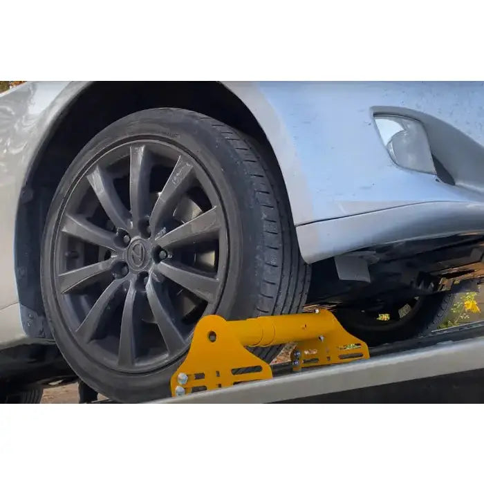 Justerbar hjulblokk fra Unitrailer, nærbilde av bilhjul mot gul metallholder på flatt underlag.