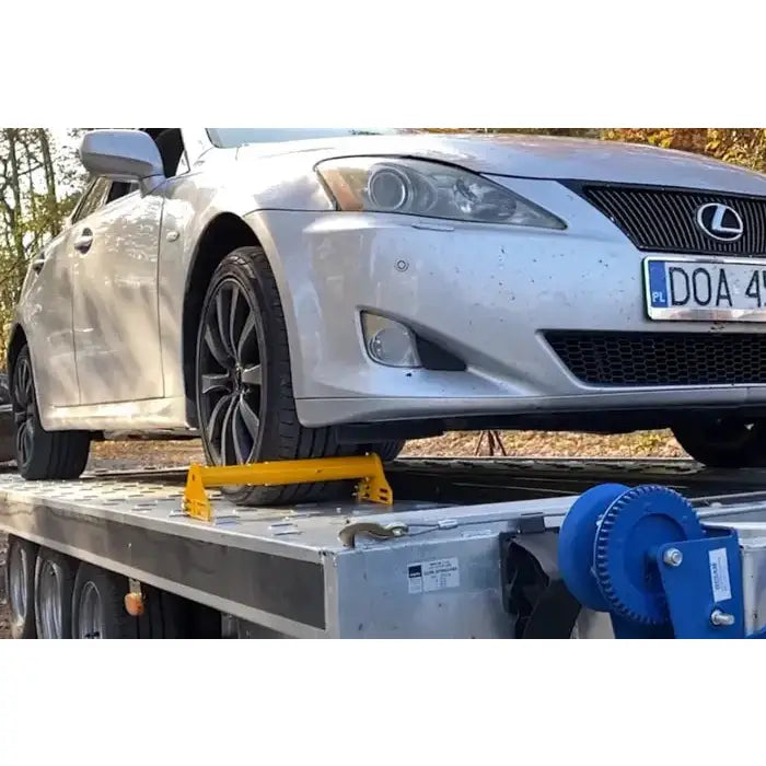 Justerbar hjulblokk fra Unitrailer, montert foran bilens dekk på tilhenger med blått vinsjehjul.