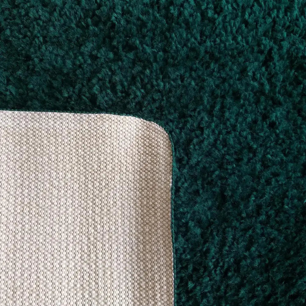 Kamel flaskegrønt teppe, nærbilde av hjørnet med loddent mørkegrønt stoff og beige vevd bakside.