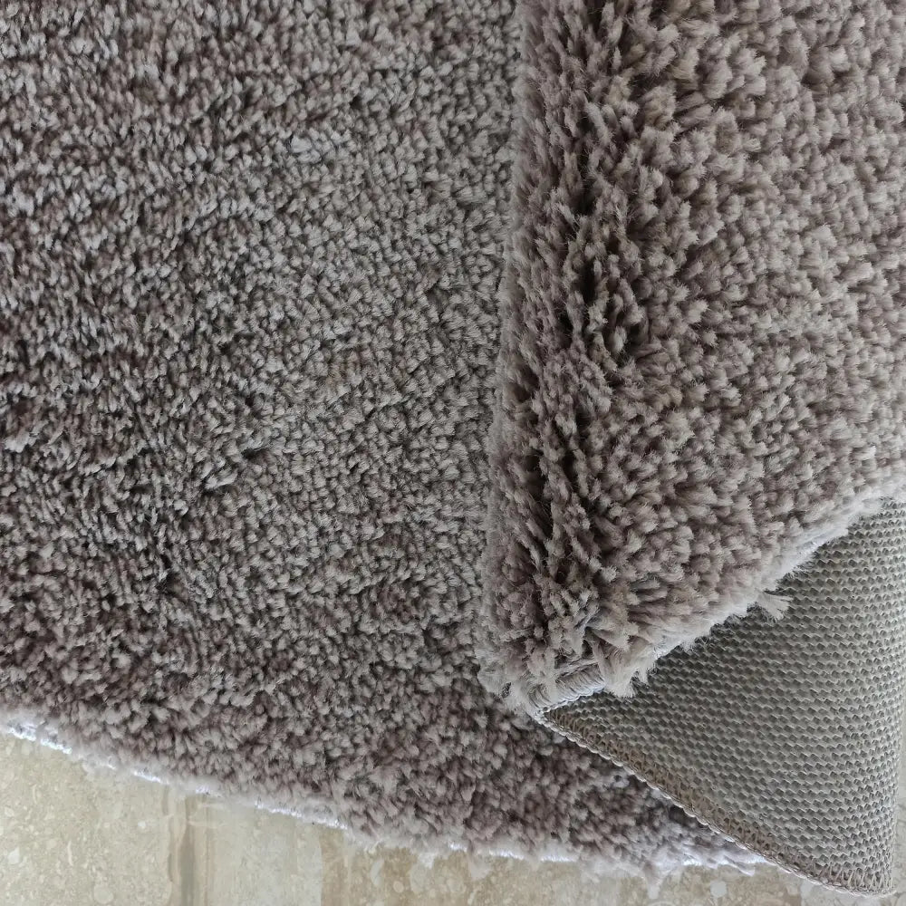 Kamel Rundt Cappuccino teppe, nærbilde av tykk, gråbrun luv og synlig bakside med tekstur.