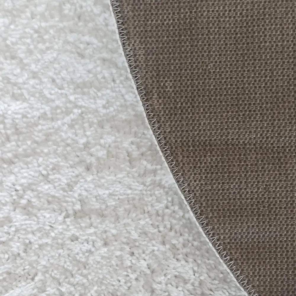 Kamel rundt hvitt teppe 200 cm, nærbilde av luftig tekstilstruktur og brun kant med synlige sømmer.