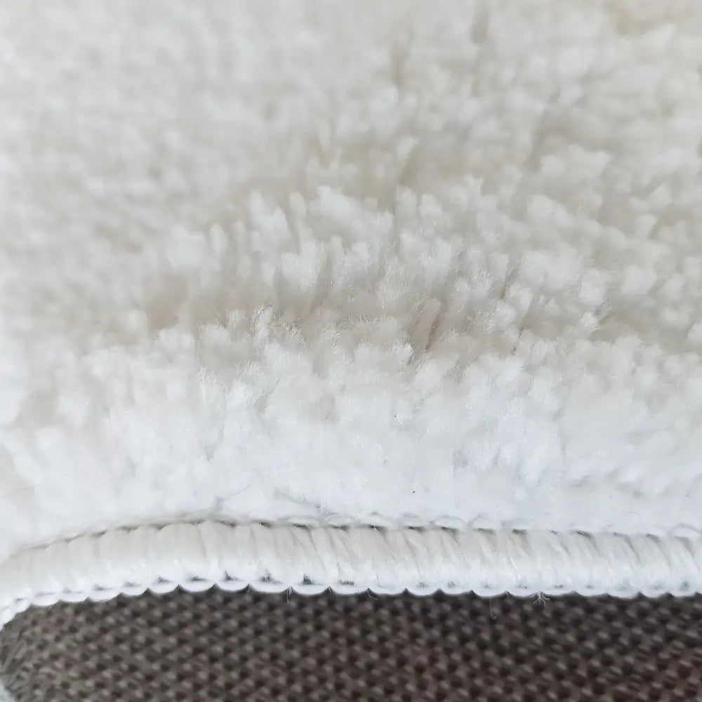 Kamel rundt hvitt teppe 200 cm, nærbilde som fremhever fiberdetaljer, sydd kant og rutete underside.