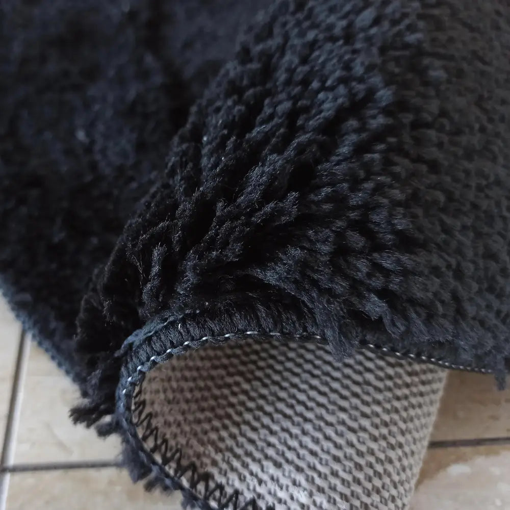 Kamel rundt svart teppe, detaljert nærbilde av den myke luggen og antiskli-undersiden på oppbrettet kant.