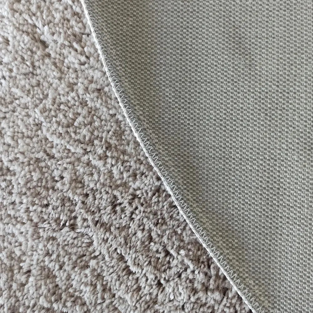 Kamel RundTepe Latte ecru, nærbilde som viser teppets myke lugg, sklisikker underside og overlock-søm.
